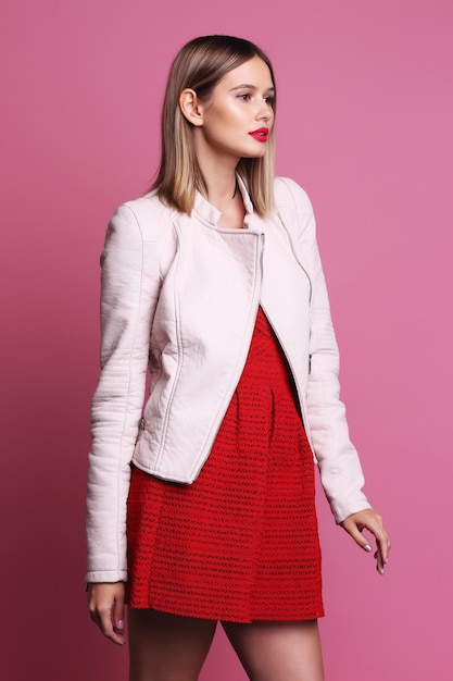 Retrato de moda de mujer joven con chaqueta de cuero rosa y vestido rojo. Fondo rosa, tiro del estudio