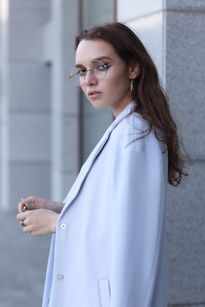 Retrato de moda de mujer joven elegante al aire libre en chaqueta, vestido, gafas. Look de moda de moda