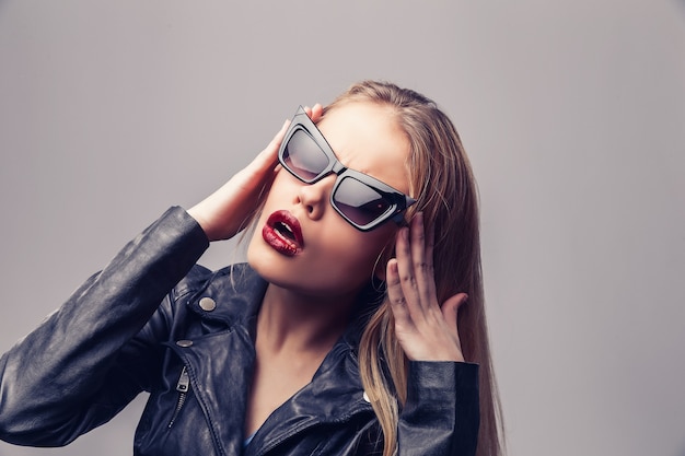 Retrato de moda de mujer joven elegante en chaqueta de cuero negro, gafas de sol.