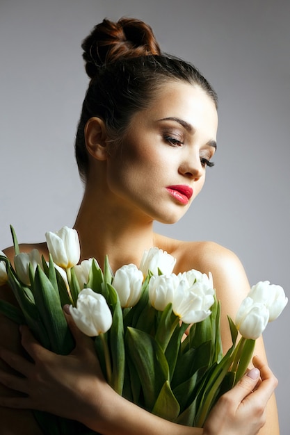 Retrato de moda de mujer joven elegante con un ramo de tulipanes blancos. Foto de estudio sobre un fondo gris.