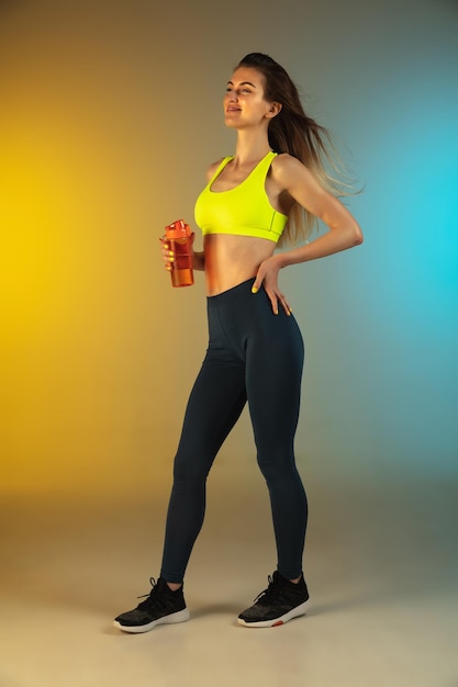 Retrato de moda de mujer joven en forma y deportiva bebiendo cócteles en gradiente