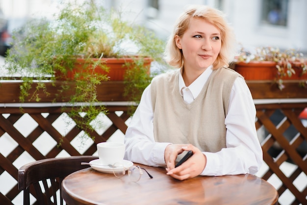 Retrato de moda de mujer joven en la mesa con una taza de café, té en la cafetería de la calle.