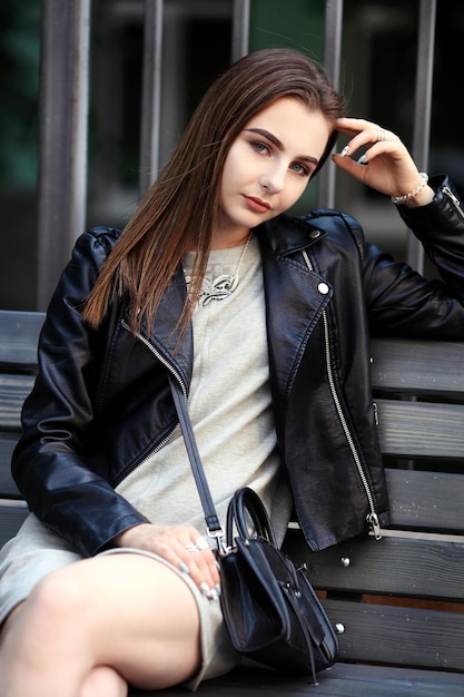 Retrato de moda de mujer morena elegante joven al aire libre chaqueta de cuero negro bolso de embrague