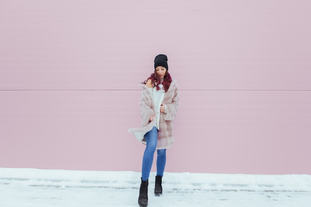 Retrato de moda de mujer muy sonriente en abrigo de visón con smartphone contra la colorida pared rosa.