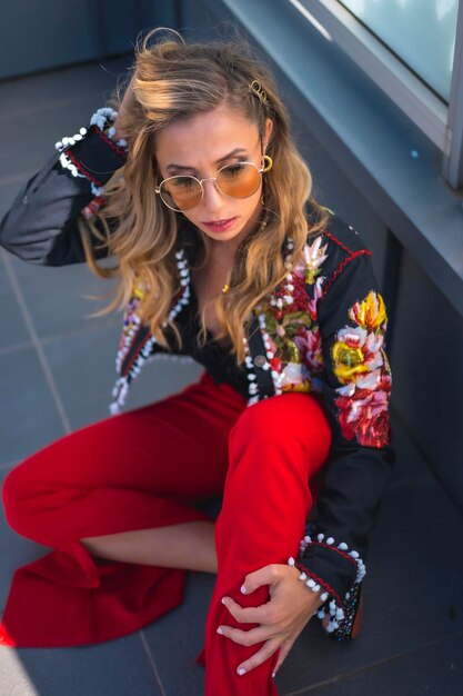 Retrato de moda de una mujer rubia en una terraza sentada en el suelo