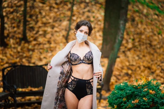 Retrato de moda de mujer sexy en mascarilla y un traje en el parque de otoño. Pandemia, virus, coronavirus