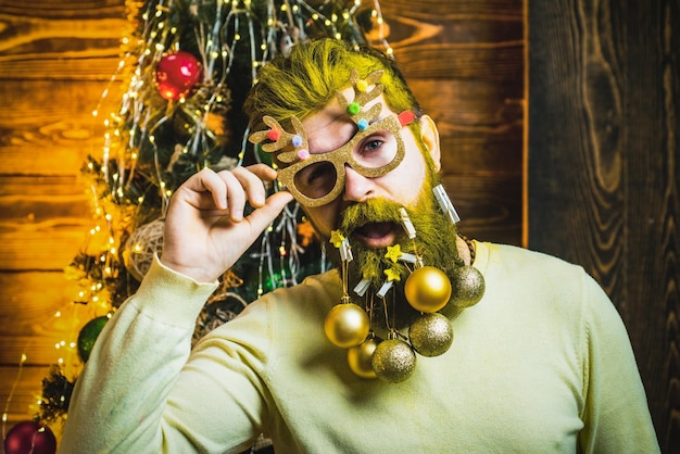 Retrato de moda de retrato de invierno de santa divertido de hombre guapo en el interior con árbol de Navidad