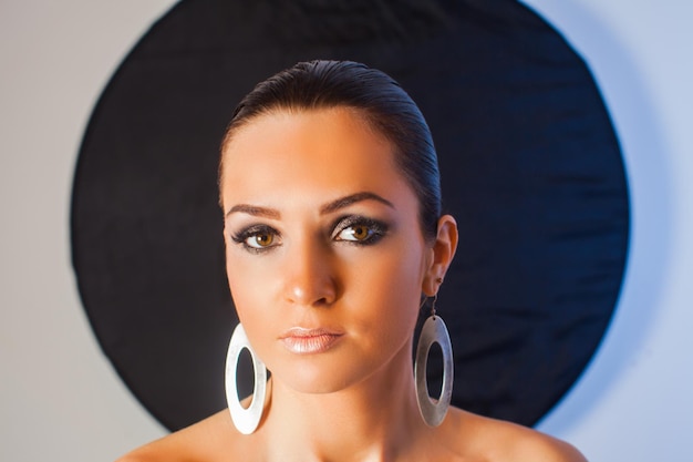 Retrato de una modelo atractiva pintada por un profesional del maquillaje con aerógrafo, que lleva grandes pendientes plateados. Primer plano de mujer con bronceado artificial mirando a la cámara