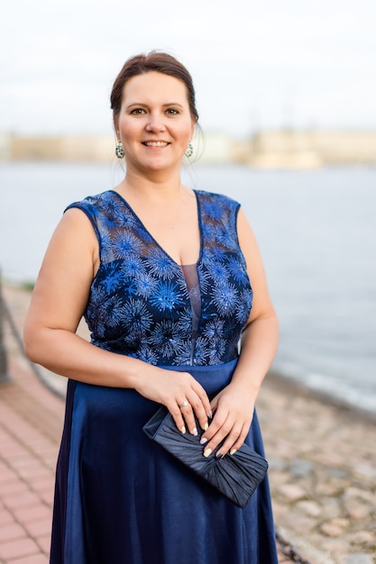 El retrato del modelo caucásico moreno sonriente en seda azul se viste en el muelle.