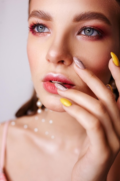 Retrato de modelo femenino con manicura con uñas largas tocando los labios y mirando hacia otro lado en el estudio