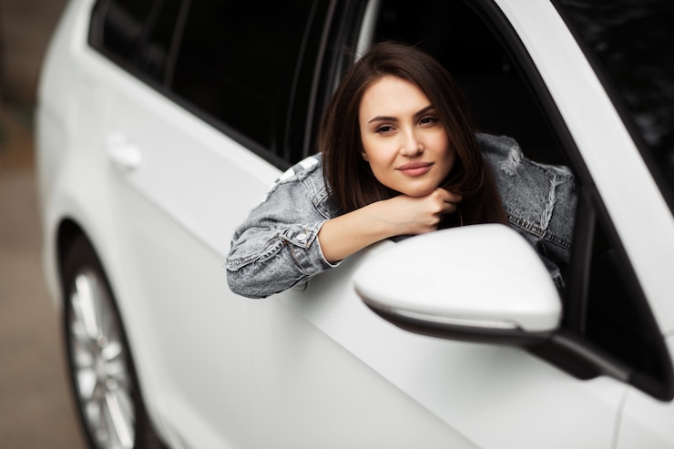 Foto retrato del modelo hermoso de la mujer morena de la moda en la chaqueta de los vaqueros que se sienta en el coche blanco de lujo.