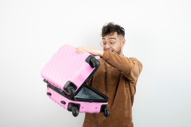 Retrato de un modelo de hombre atractivo de pie y sosteniendo una bolsa de viaje rosa.