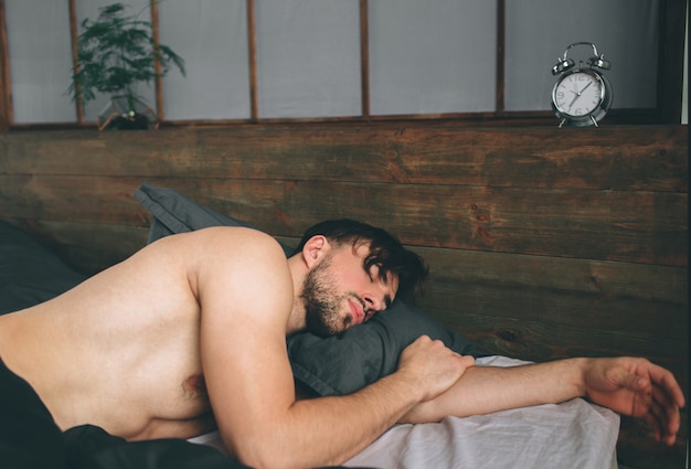 Retrato de modelo masculino en forma dormida en lujosa habitación bañada por la luz de la ventana brillante mañana cálida