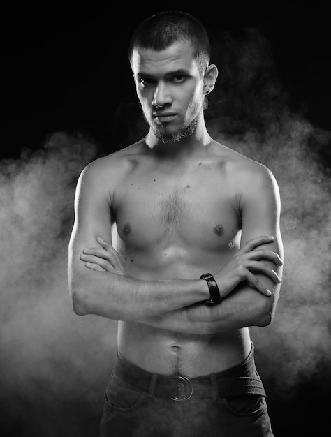 Retrato de un modelo masculino musculoso contra un fondo oscuro con humo.