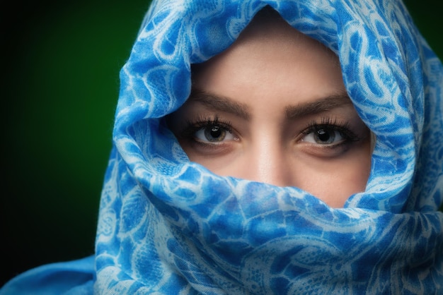 Retrato de una modelo de moda cubriendo la cara con una bufanda contra un fondo de color