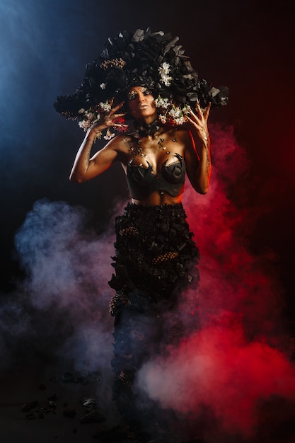 Retrato de una modelo con tocado y vestido de carbón. Hay humo rojo detrás del modelo.