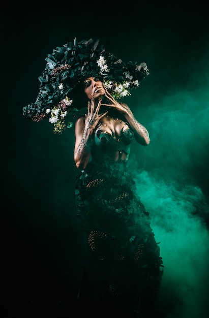 Retrato de una modelo con tocado y vestido de carbón. Hay humo verde detrás del modelo.