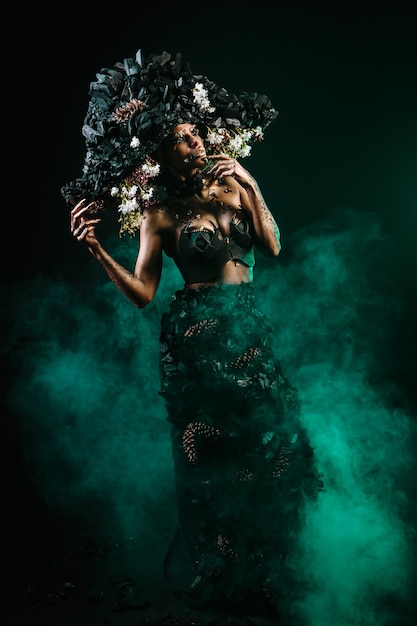 Retrato de una modelo con tocado y vestido de carbón. Hay humo verde detrás del modelo.