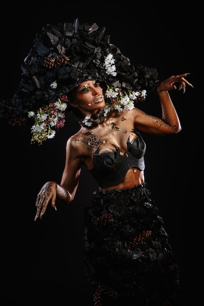 Foto retrato de una modelo con tocado y vestido de carbón. maquillaje brillante y arte corporal.