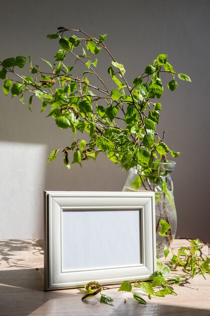 Retrato moldura branca na mesa de madeira Vaso de vidro moderno com ramos verdes Eco estilo de vida