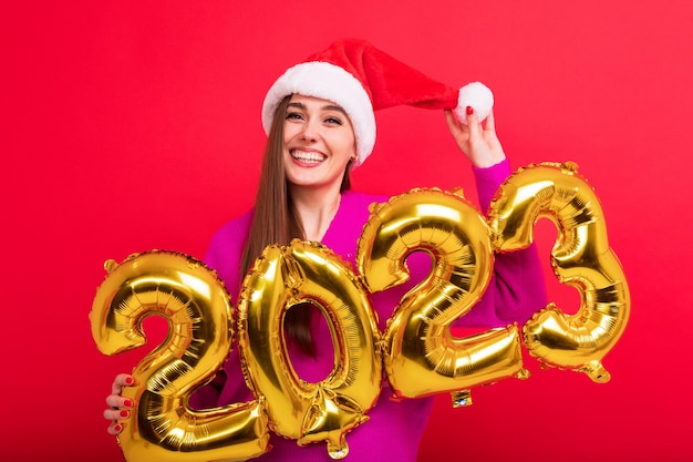 Un retrato de una morena de buen humor sostiene las figuras del nuevo año 2023 Una mujer joven se puso un sombrero de Papá Noel