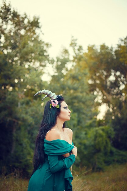 Retrato de una morena con una corona de flores en la cabeza, cuernos en el bosque.