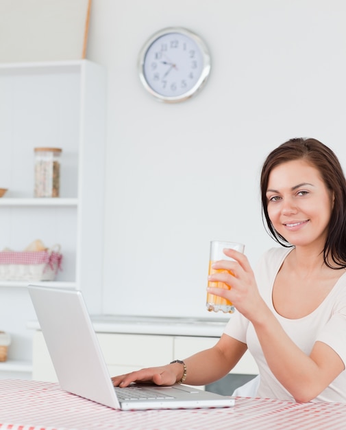 Retrato de una morena con su computadora portátil y beber jugo