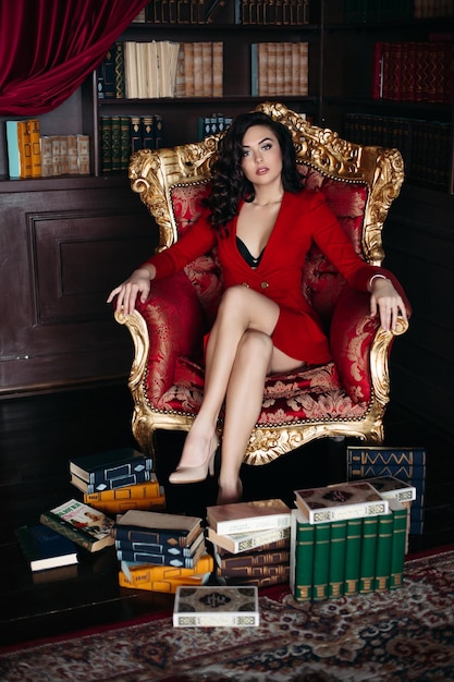 Retrato de morena con vestido rojo sentada en un sillón en el interior de la biblioteca