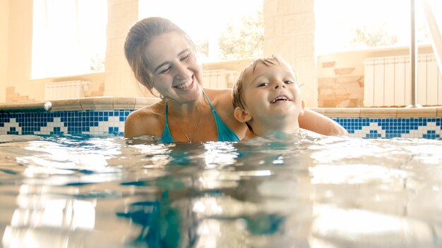 Retrato de mothet joven alegre feliz con niño de 3 años jugando en la piscina de la casa. Niño aprendiendo a nadar con sus padres. Familia divirtiéndose en verano