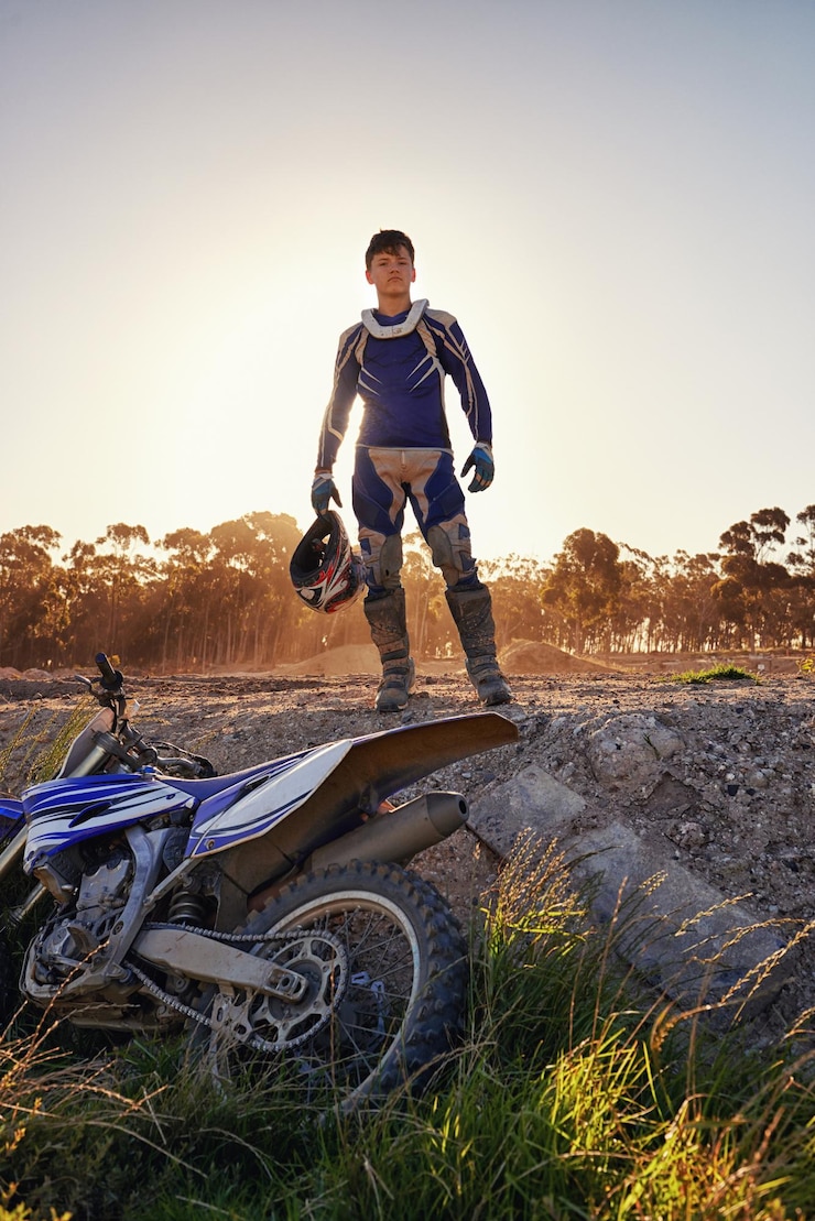 Foto retrato de motocross y piloto de dirtbike en el bosque confiado y deporte extremo para la aventura con velocidad hombre orgullo o equipo para carreras de motocicletas en pista puesta de sol o habilidad en la conducción de un vehículo rápido