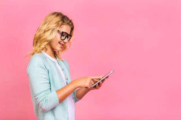 Retrato de muchacha adolescente niño lindo que se encuentran aisladas sobre fondo rosa mediante teléfono móvil.