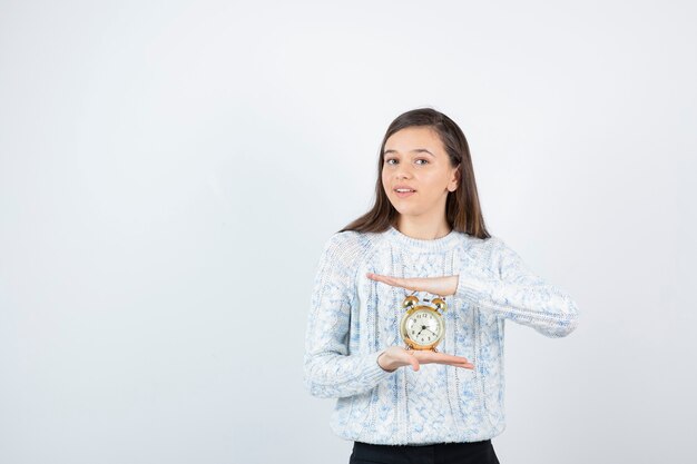 Retrato de muchacha adolescente en suéter con reloj despertador.