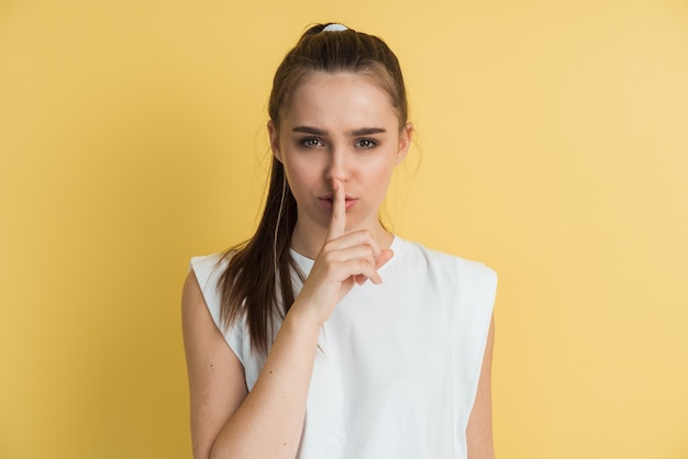 Retrato de muchacha atractiva con el dedo en los labios, aislado sobre fondo amarillo.