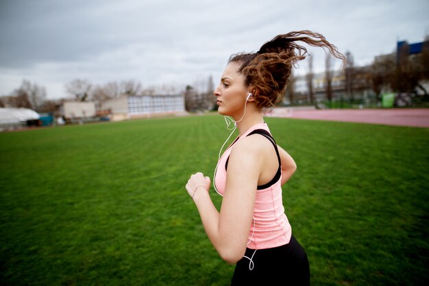 Retrato de la muchacha atractiva joven feliz de la aptitud que activa mientras que escucha la música afuera en pista de atletismo.