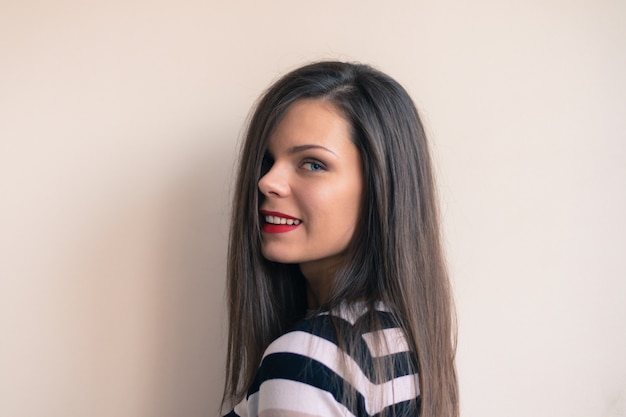 Retrato de una muchacha bonita joven con el pelo largo y el lápiz labial rojo en un fondo beige