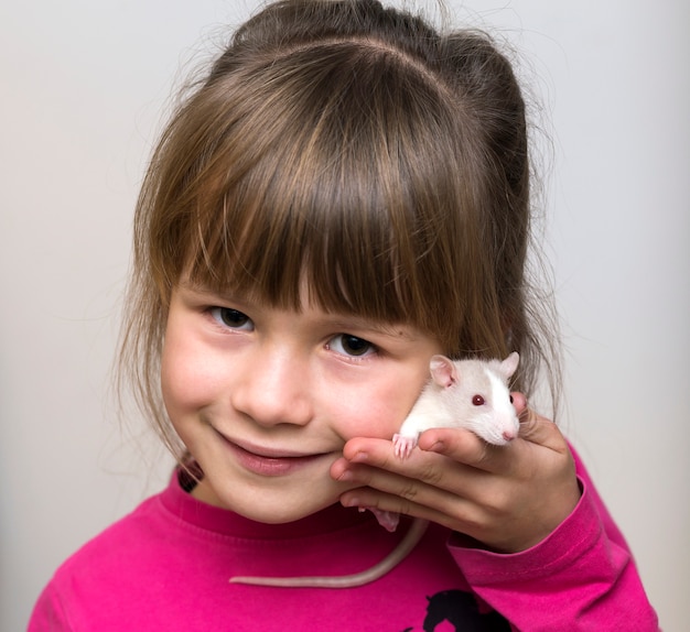 Retrato de la muchacha feliz sonriente del niño lindo con el hámster blanco del ratón del animal doméstico en fondo del espacio de la copia ligera. Mantener a las mascotas en casa, cuidar y amar al concepto de animales.