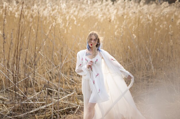 Retrato de una muchacha hermosa joven en el vestido blanco en el campo de trigo, caminando, despreocupado.