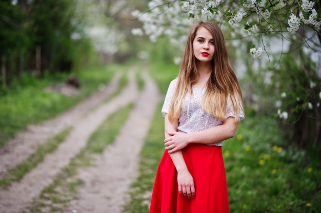 Retrato de muchacha hermosa con labios rojos en el jardín de flor de primavera, use vestido rojo y blusa blanca.