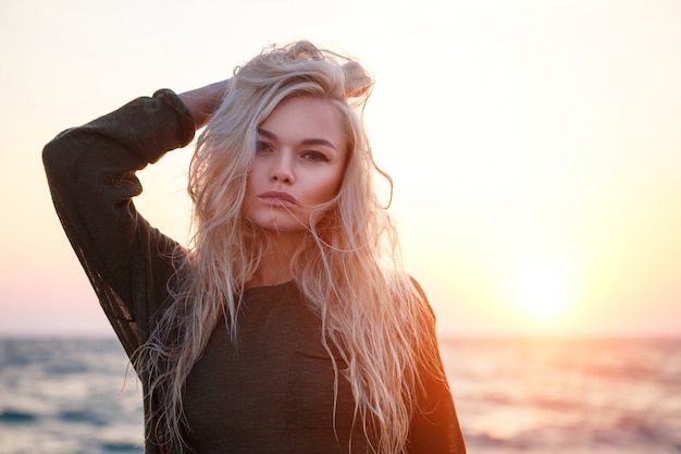 Retrato de una muchacha hermosa en la playa en la puesta del sol.