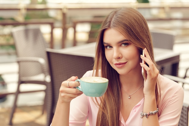 Retrato de muchacha hermosa con su teléfono móvil en la cafetería.