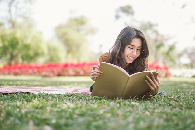 Foto el retrato de la muchacha de la high school secundaria se acostó y leyó un libro en parque.