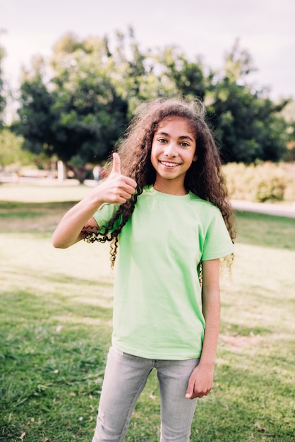 Retrato de una muchacha con los pelos rizados que muestran el pulgar que se levanta en parque