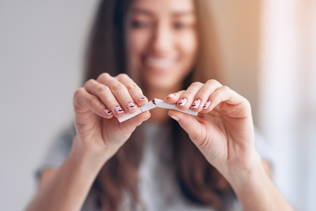 Retrato de la muchacha sonriente hermosa que sostiene el cigarrillo roto en manos. Feliz mujer dejar de fumar cigarrillos. Dejar el mal hábito, el concepto de atención médica. No Fumar.