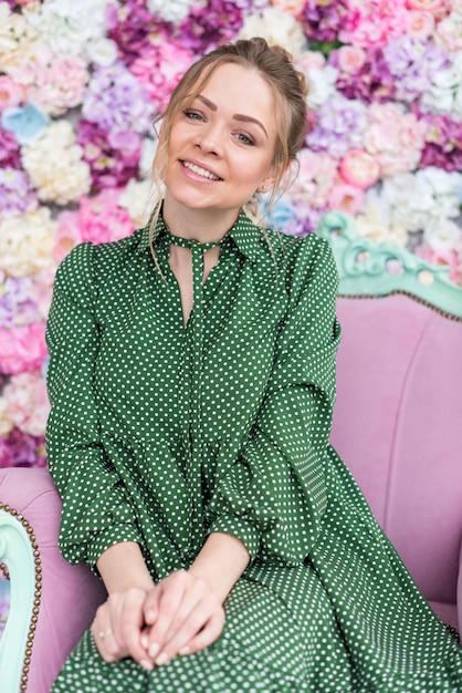 El retrato de la muchacha tímida rubia se sienta en la silla contra un fondo floral