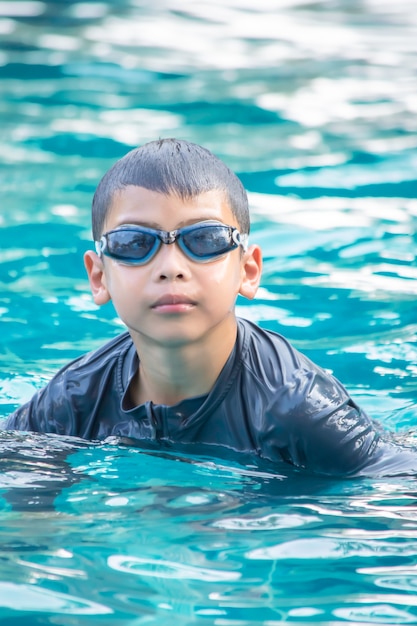 Retrato muchacho asiático con gafas de natación en la piscina.