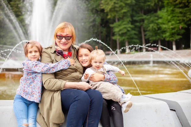 Retrato de una mujer de 65 años con nietas en el fondo de una fuente en el parquexDxA