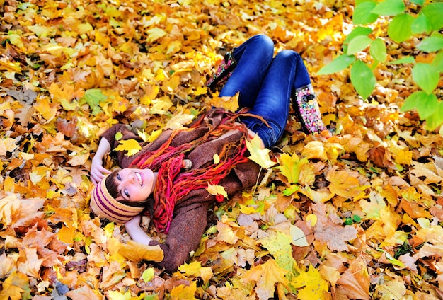 Retrato de mujer acostada sobre hojas de otoño en el parque.