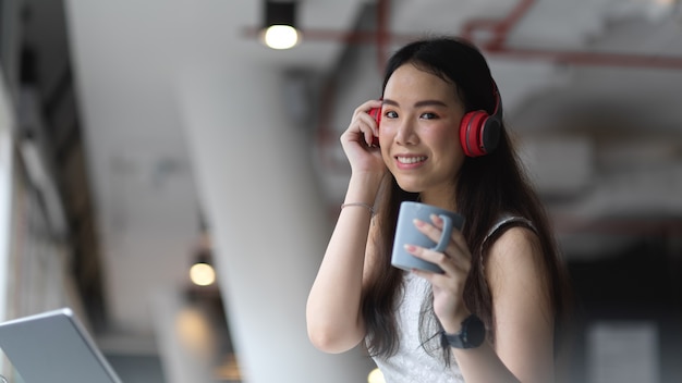 Retrato de mujer adolescente escuchando música con auriculares y relajándose con un café en la cafetería