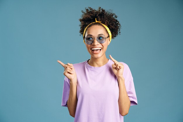 Retrato de mujer adolescente sorprendida con los dedos justo en el espacio vacío, mientras mira hacia otro lado con la boca abierta y expresión de asombro. Tiro de estudio interior aislado sobre fondo rosa