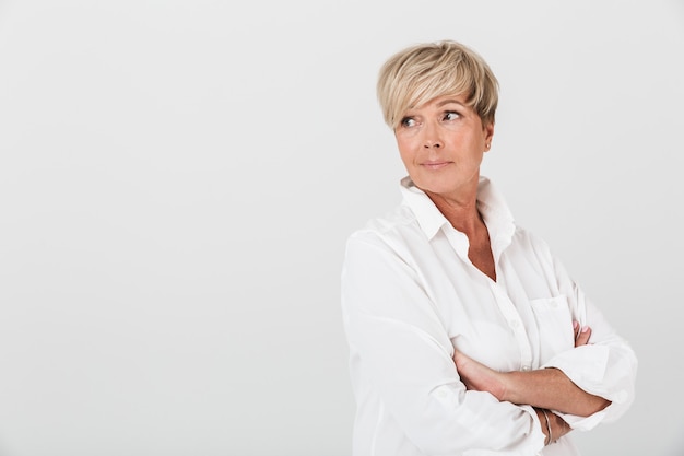 Foto retrato de mujer adulta caucásica mirando copyspace con los brazos cruzados aislado sobre una pared blanca en el estudio